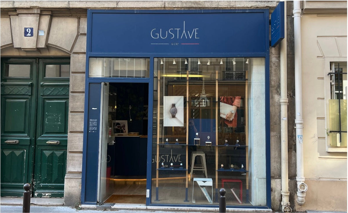 Façade bleue de la boutique Gustave & Cie au 2 Rue Bénard à Paris. Vitrine en bois exposant des montres sous une enseigne blanche sur fond bleu.