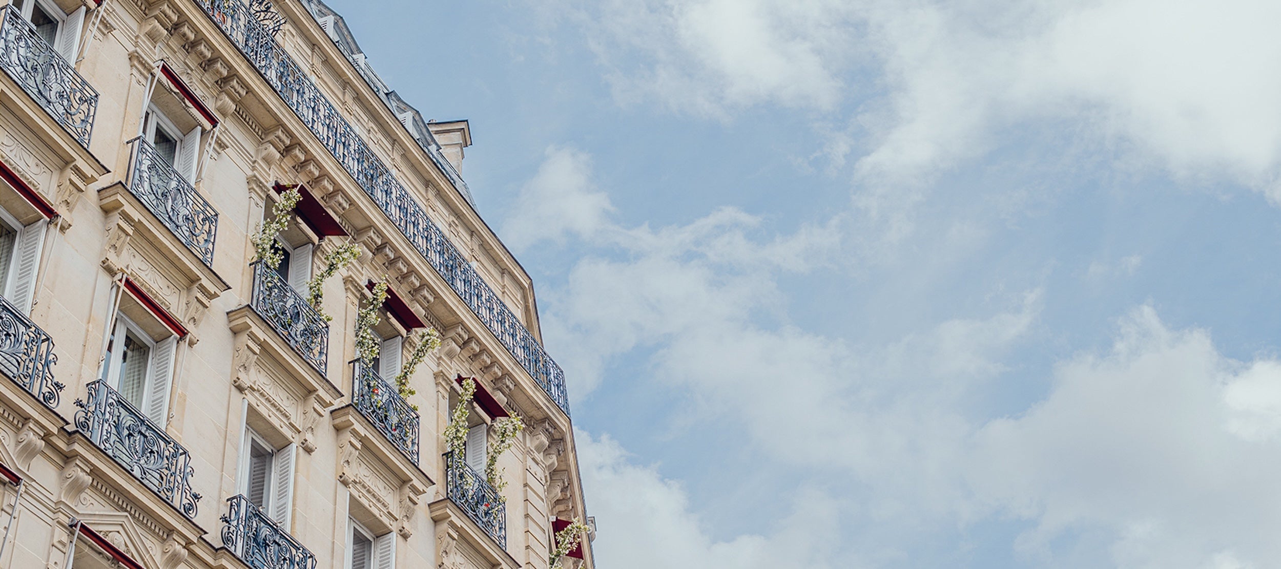 Vue en contre-plongée d’un immeuble haussmannien parisien se détachant sur un ciel bleu parsemé de nuages.