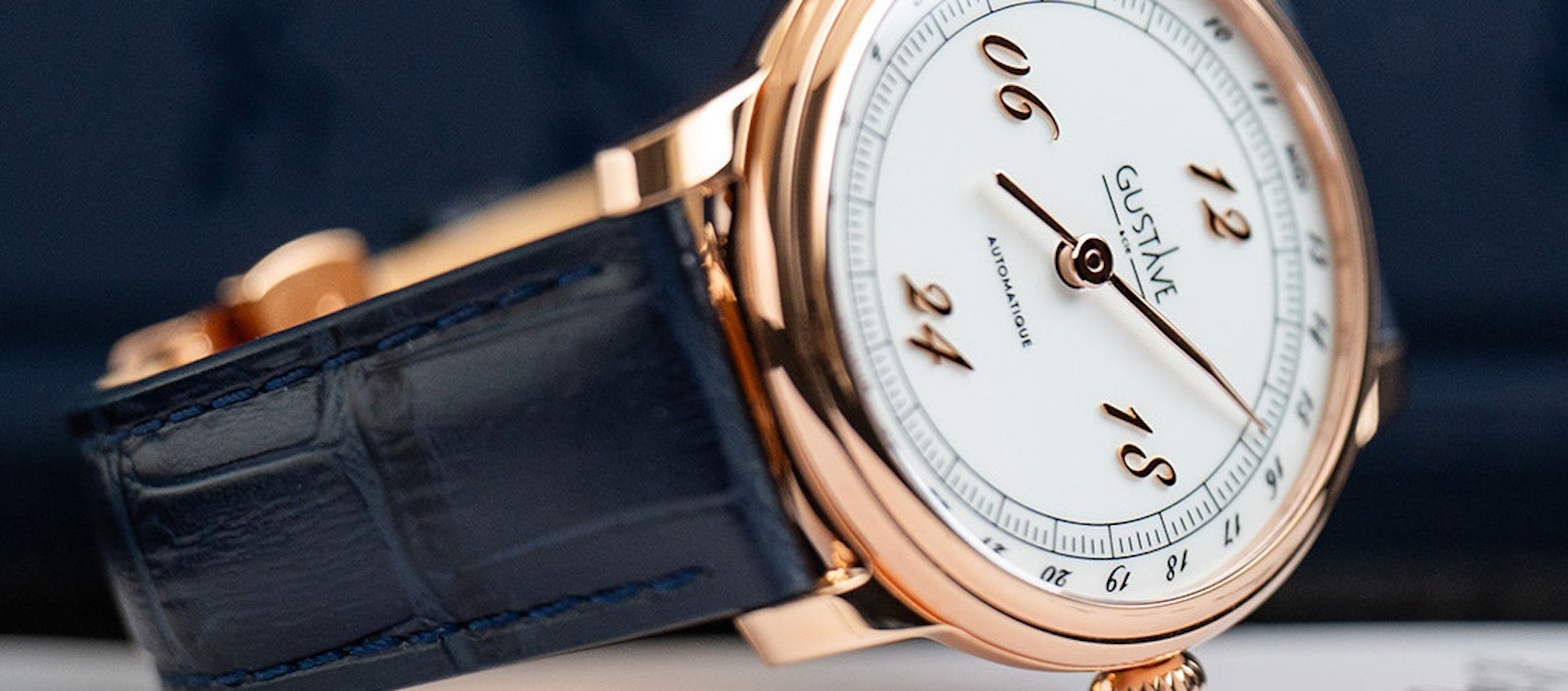 Montre automatique Gustave & Cie Paul 24H avec boîtier finition or rose PVD, cadran blanc, verre saphir et bracelet en cuir bleu façon crocodile.