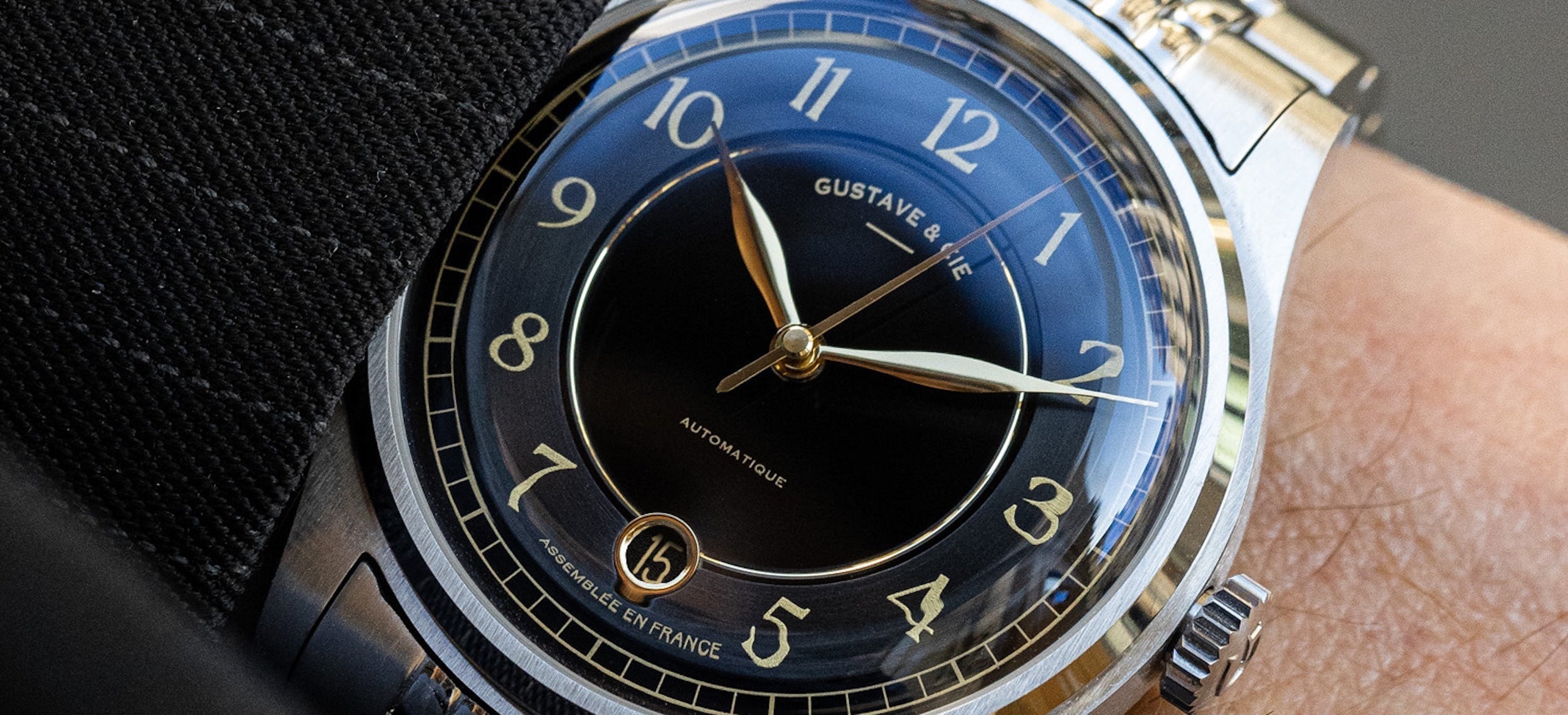 Montre automatique Gustave & Cie Charles 12H avec boîtier argenté, cadran noir, verre saphir et bracelet acier grain de riz, portée au poignet.
