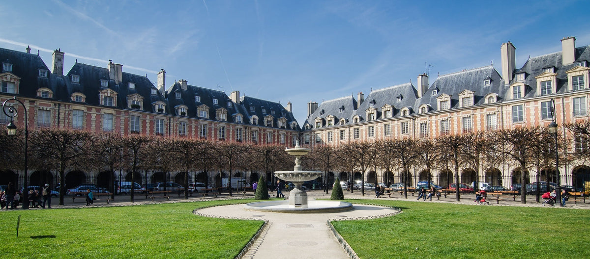 Vue de la Place des Vosges : pelouse, fontaine et immeubles symétriques en briques rouges aux toits d'ardoise caractéristiques au cœur de Paris.